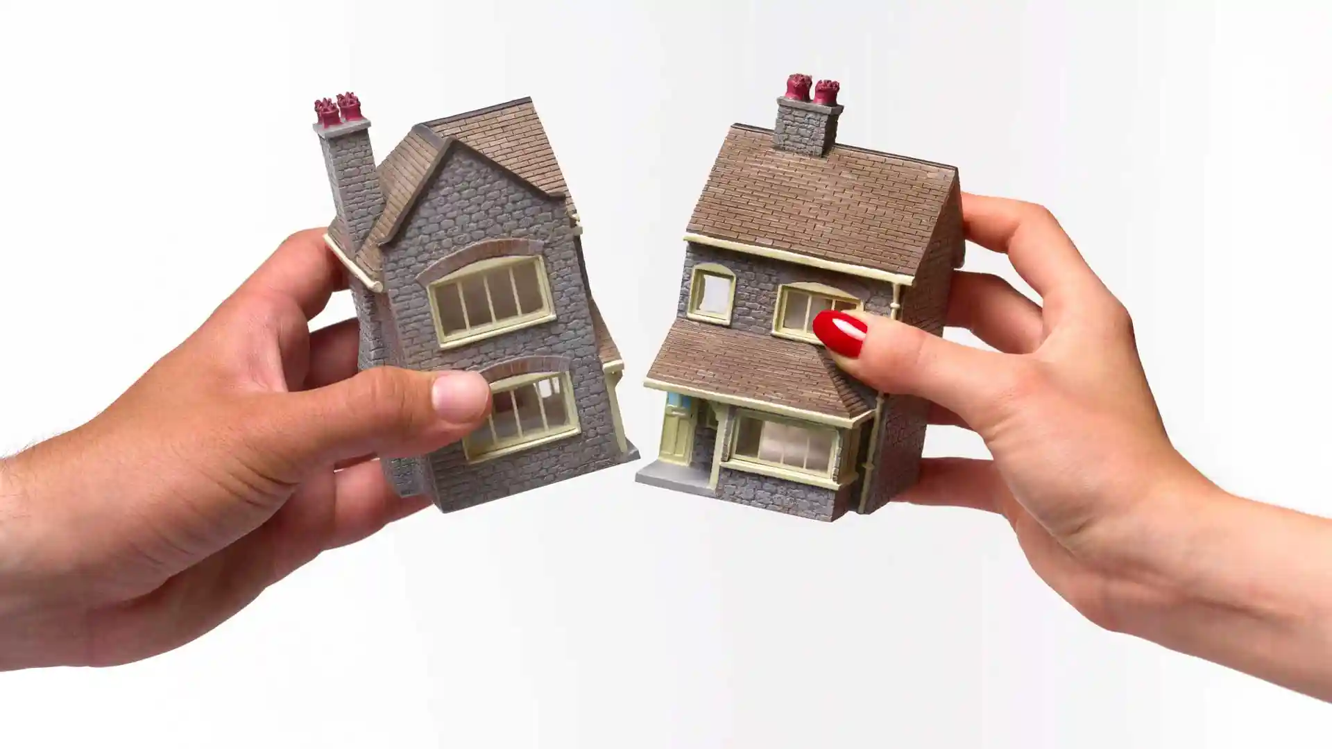 Photo of a miniature home being split by two different hands.